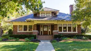 Front view of a Craftsman bungalow with a broad porch, exposed rafters, and brick piers.