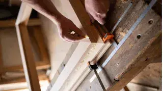 Hands assembling a DIY wood window frame on a country workshop bench.