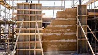 Rammed earth wall between formwork panels on a braced construction site.
