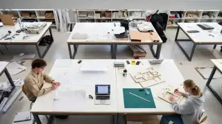 Architecture students working in a design studio with drawings, models, and critique boards.