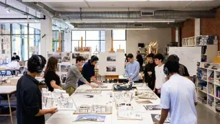 Architecture students reviewing models and drawings in a professional studio.