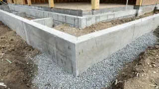 Poured concrete house foundation corner with gravel base at a residential jobsite.
