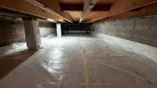Installed crawl space vapor barrier with taped seams, wall turn-up, and wrapped piers.