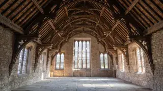 Gothic hall interior with exposed timber roof and long stone-walled room.