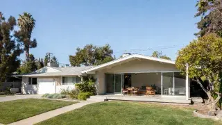 Modern addition to a ranch house with a new gabled living volume and wide sliding glass opening.