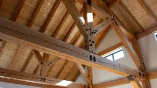 Exposed timber roof truss with heavy beams, braces, and visible steel connectors.