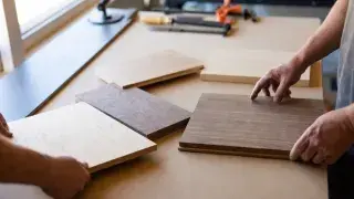Wood boards laid out for comparison on a workshop table while hands evaluate grain, color, and type.