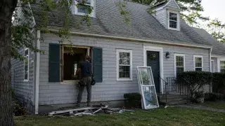 Cape Cod house during window replacement with an open window bay and worker outside.