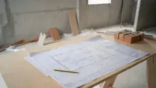 Architectural floor plan on a plywood table at an unfinished construction site.