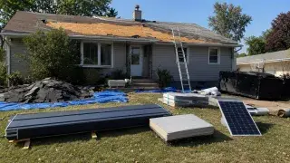 House roof replacement with exposed sheathing, staged metal roofing, reflective roofing, and solar panel planning materials.