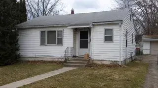 Plain 1950s bungalow exterior before renovation with dated siding, small stoop, and modest windows.