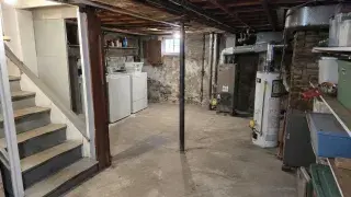 Cape Cod basement before guest-suite planning with low ceiling, laundry, ducts, posts, and utilities.