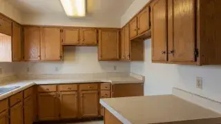 Dated empty kitchen with oak cabinets, laminate counters, and fluorescent lighting.