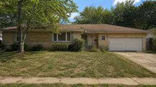 Dated brick ranch house with an attached garage, overgrown shrubs, and a worn front yard.