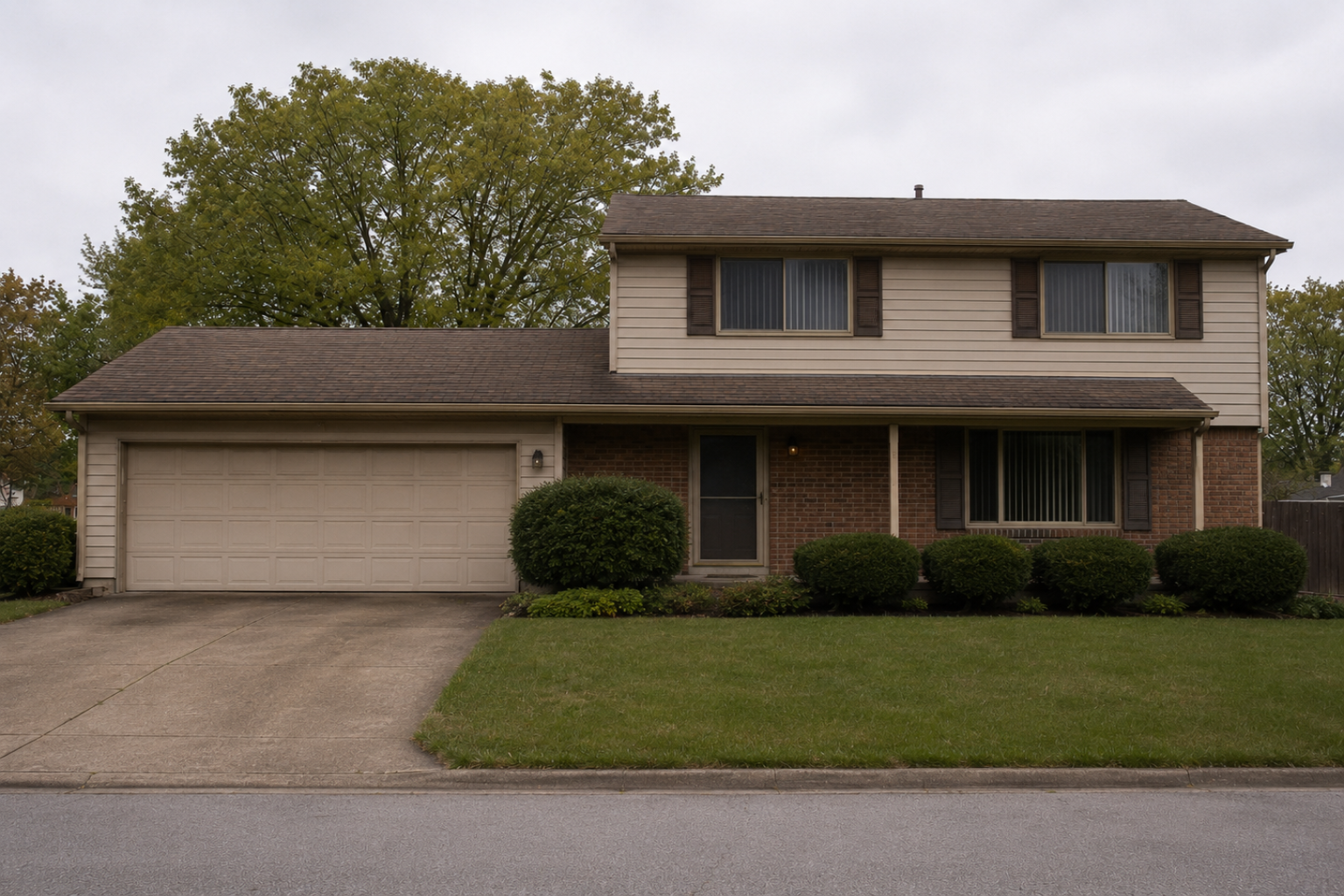 1980s suburban house exterior with beige siding, brick veneer, brown shutters, garage, lawn, and shrubs.
