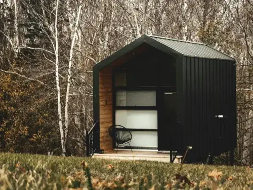 A sleek modern tiny house located on the edge of a forest.