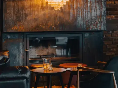 Rustic living room with a fireplace, wall behind it featuring chandeliers and armchairs nearby.