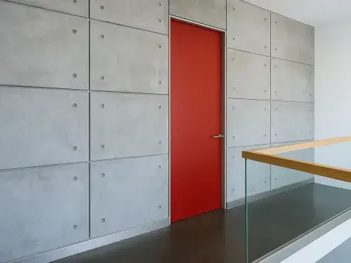 Modern loft interior with bold red door in concrete wall and glass railing.