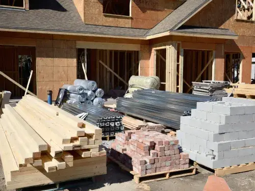 Common building materials including lumber, brick, concrete block, steel, and insulation at a residential jobsite.