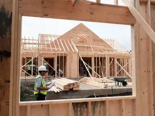 Construction manager reviewing plans at active house framing site for Construction Management.