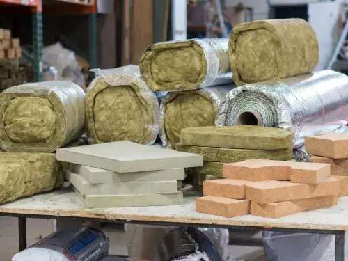 Mixed insulation materials on a workshop table, including batts, rigid foam, and foil-faced rolls.