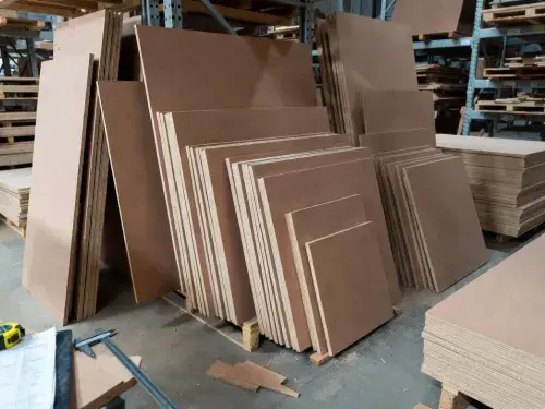Stacked MDF sheets in various sizes and thicknesses on warehouse pallets with measuring tools.