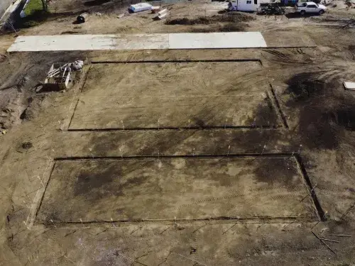Prepared residential building site with layout stakes, early access concrete, and graded ground before construction starts.