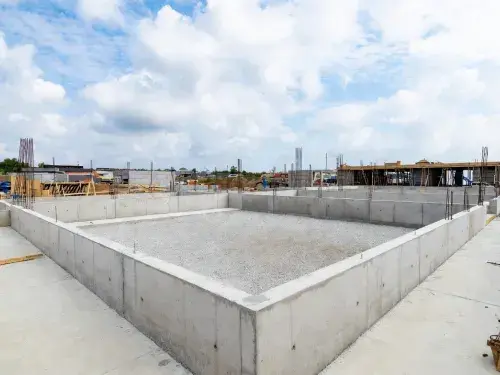 Reinforced concrete foundation enclosure with gravel base and vertical reinforcing bars on site.