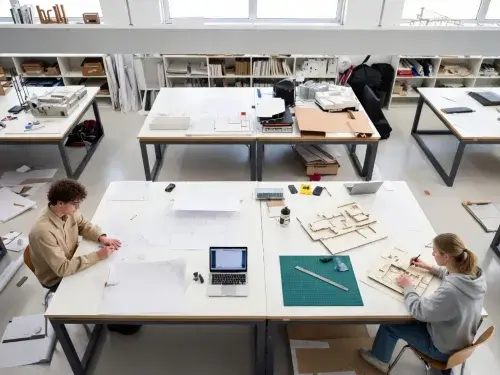 Architecture students working in a design studio with drawings, models, and critique boards.