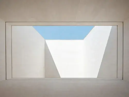 Framed architectural void formed by white concrete walls and layered openings to the sky.