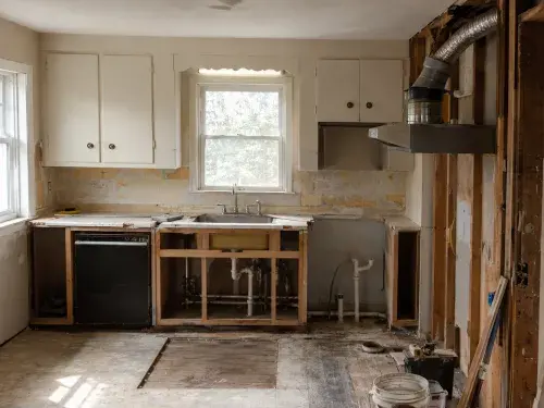 1950s kitchen remodel in progress with exposed wall framing, plumbing, ductwork, old cabinets, floor layers, and unfinished repair areas.