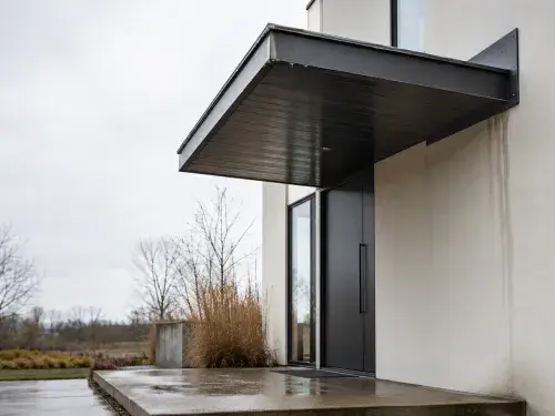 Modern entry canopy with water staining at the wall connection and a wet concrete slab below.