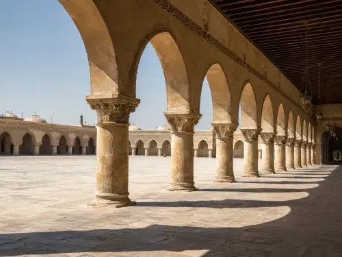 Islamic arcade with repeated stone arches casting shade across a courtyard walkway.