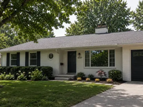 Updated ranch house exterior with white brick, black shutters, a dark garage door, low roofline, and restrained front landscaping.