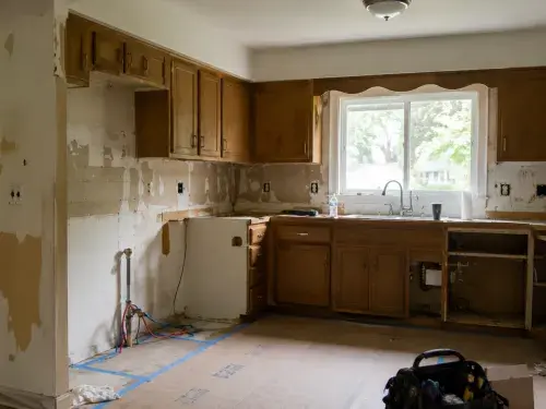 Ranch house kitchen renovation with older cabinets, exposed wall areas, rough-in work, and protective floor covering.