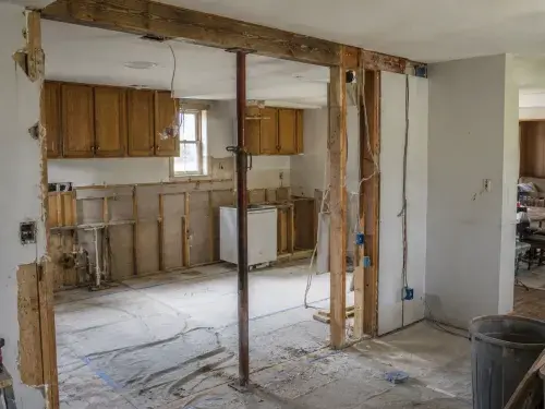Ranch kitchen wall removal with temporary support, exposed studs, beam area, wiring, protected floor, and living room beyond.