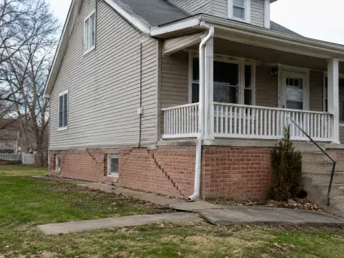 Older house with brick foundation cracks, uneven walkway, and visible signs of foundation settlement.