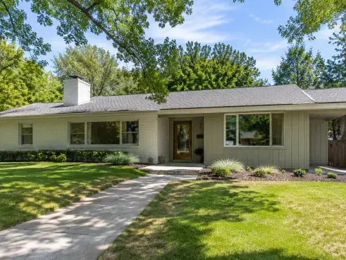 Updated 1960s ranch house exterior with low roofline, painted brick, vertical siding, simple entry, broad front windows, and restrained landscaping.