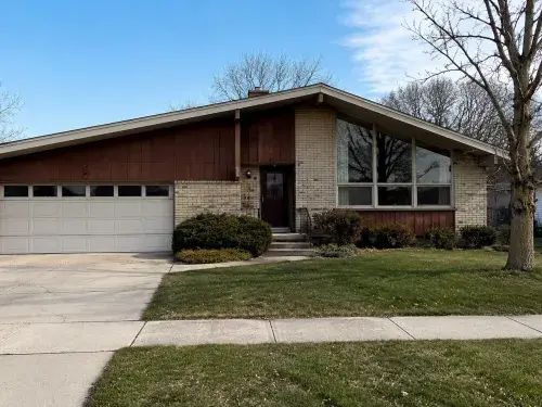 Modest 1970s suburban house with brick, wood siding, attached garage, and dated entry.