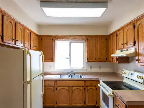 1980s kitchen with oak cabinets, almond appliances, laminate counters, and fluorescent ceiling light.