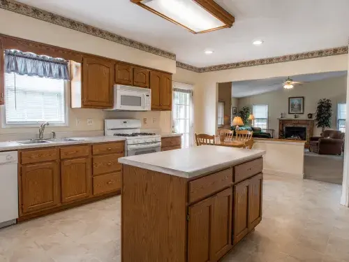 1990s kitchen before remodel with oak cabinets, laminate counters, island, and dated lighting.