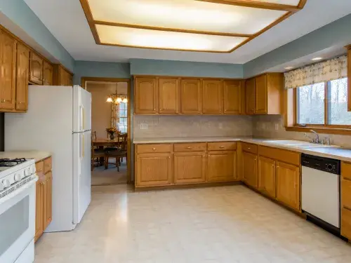 1990s kitchen with honey oak cabinets, laminate counters, white appliances, and dated lighting.