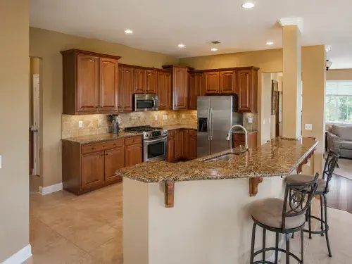 Early 2000s builder kitchen with cherry cabinets, brown granite, tile floor, and open family room.