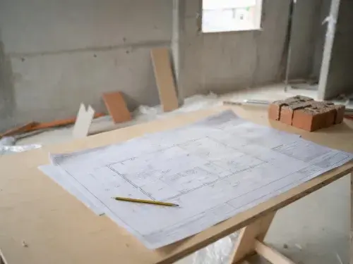 Architectural floor plan on a plywood table at an unfinished construction site.