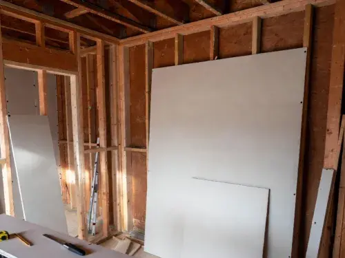 Drywall sheets staged in a renovation room before installation with exposed framing and layout tools.