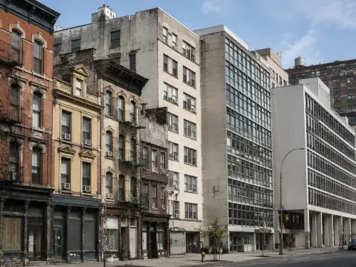 City street showing older masonry buildings beside cleaner early modern buildings with glass, steel, and concrete facades.
