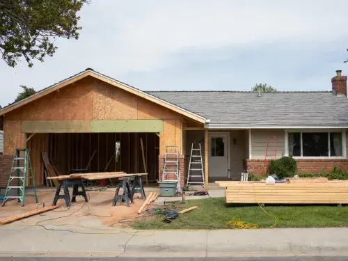 Ranch house with a front garage addition under construction and driveway materials on site.