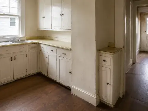 Unrenovated 1920s bungalow kitchen with worn cabinets, laminate counters, and a narrow layout.