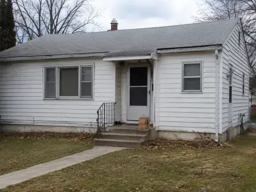 Plain 1950s bungalow exterior before renovation with dated siding, small stoop, and modest windows.
