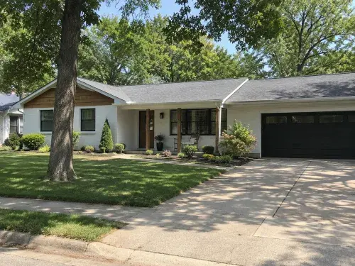 Renovated 1980s ranch house with attached right-side garage and shaded front lawn.